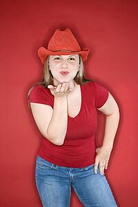 Young Caucasian female adult blowing kiss wearing red cowboy hat.