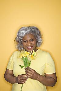 African American female mature adult holding flowers looking at viewer smiling.