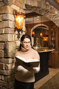 Caucasian woman standing in front of kitchen holding book and reading.