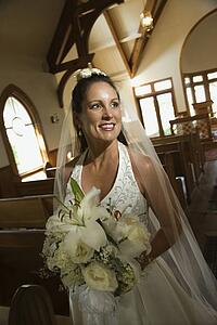 Portrait of mid-adult bride holding bouquet leaving a church. 
