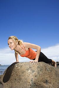 Caucasian young adult woman doing push up on rock.