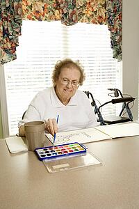 Elderly Caucasian woman painting with watercolors at retirement community center.