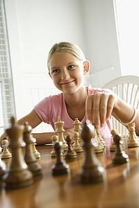 Caucasian pre-teen girl playing chess smiling.