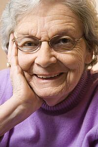 Elderly Caucasian woman smiling with hand on face.