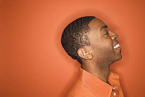 Side view of smiling young African-American man on orange background.
