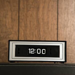 Retro clock set for 12: 00 against wood paneling.