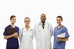 Portrait of African-American man and Caucasian women medical healthcare workers smiling in uniforms standing against white background.