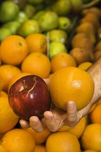 Close-up of Caucasian male hand holding apple and orange.
