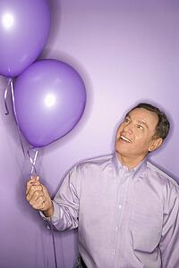 Smiling middle-aged Caucasian man on purple background holding purple balloons.