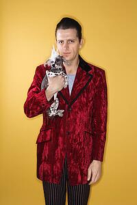 Caucasian mid-adult male wearing velvet holding Chinese Crested dog.