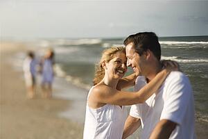 Caucasian mother and father having romantic moment on beach with children in background.