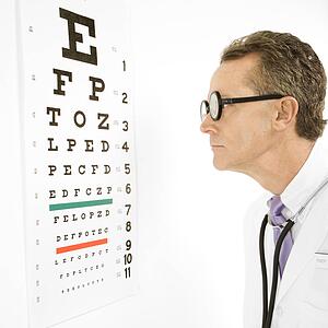 Mid-adult Caucasian male doctor wearing eyeglasses looking at an eye chart.