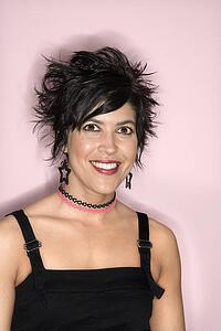 Head and shoulder portrait of smiling Hispanic woman against pink background.