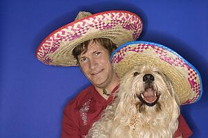 Fluffy brown dog and Caucasian male young adult wearing Mexican sombreros.