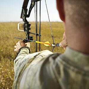 Bow hunter in field pulling back arrow on compund bow.