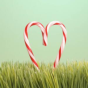 Still life of two upright candy canes forming a heart in the grass.