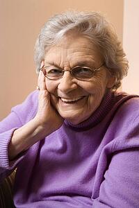 Elderly Caucasian woman smiling with hand on face.