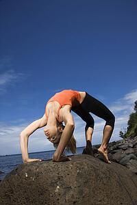 Caucasian young adult woman doing yoga on rocky shore.