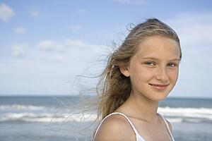 Caucasian pre-teen girl on beach looking at viewer.