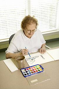 Elderly Caucasian woman painting with watercolors at retirement community center.