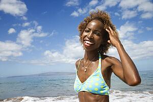 Mid-adult Black female smiling and touhing hair with ocean in background.