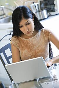 Asian/Indian young woman sitting at table working on laptop computer.