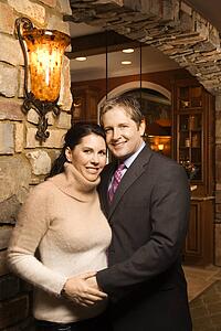 Caucasian woman and Caucasian man with arms around each other looking at viewer and smiling.