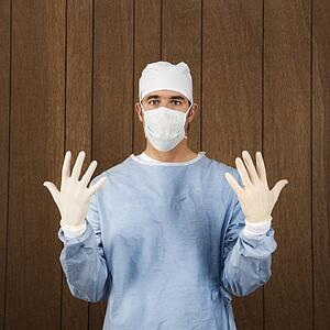 Caucasian mid-adult male surgeon wearing face mask and holding up gloved hands.