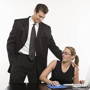 Caucasian mid-adult man sexually harassing woman sitting at computer.