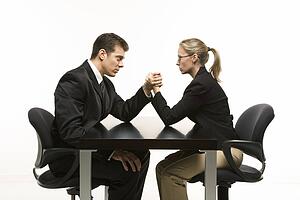 Side view of Caucasian mid-adult businessman and businesswoman arm wrestling on table.