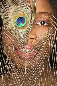 Close-up smiling African-American mid-adult woman looking through peacock feather.