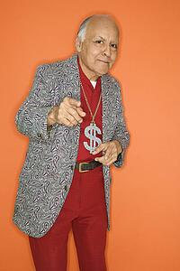 Mature adult Caucasian male wearing money sign necklace and pointing.
