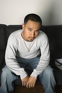 Asian young adult man sitting on sofa looking at viewer with critical expression.