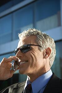 Close up side view of prime adult Caucasian man in suit talking on cellphone in urban setting.