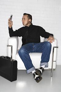 Caucasian mid-adult man with tattoos and piercings looking at cell phone with briefcase.