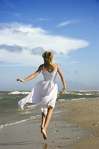 Caucasian pre-teen girl running down the beach in flowing white dress.