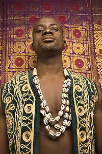 Low angle portrait of African-American mid-adult man wearing embroidered African vest and beads.