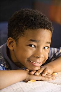 Portrait of young smiling boy with head on hands with book in front looking at viewer.