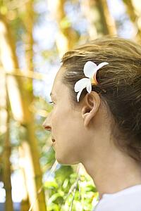 Caucasian mid-adult woman wearing plumeria flower behind ear.