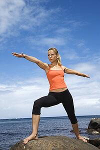 Caucasian young adult woman doing yoga on rocky shore.