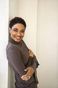 African-American woman standing leaning against wall smiling looking at viewer with arms crossed.