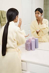 Asian/Indian young woman looking in mirror applying facial scrub.