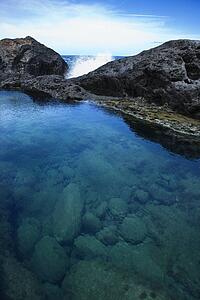 Tidal pool with wave crashing on rocks in background with blue sky in Maui, Hawaii, USA.