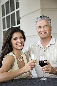 Prime adult Hispanic female and Caucasian prime adult male toasting sitting at table.