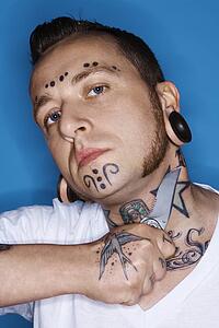 Caucasian mid-adult man with tattoos and piercings holding knife to throat.