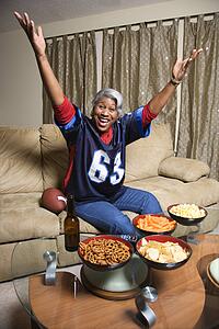 Portrait of a Middle-aged African-American woman wearing a football jersey with hands in the air watching football game. 