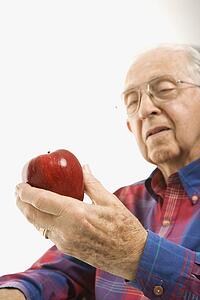 Caucasion elderly man looking at red apple in his hand.