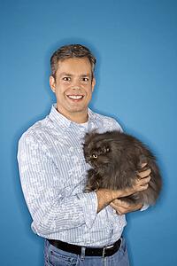 Mid-adult Caucasian man standing holding Persian cat.