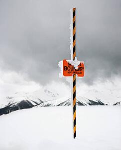 Ski area trail boundary sign in snow-covered mountain scene.