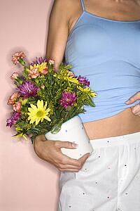Detail of Caucasian female holding pot of flowers at hip.